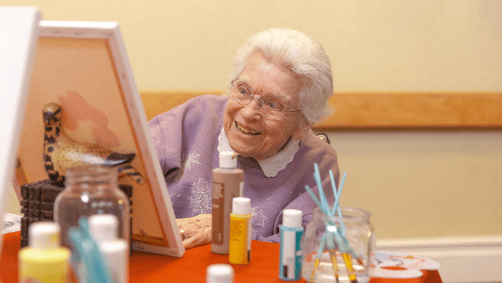 Senior smiling in an independent living community being socially active and painting during an activity